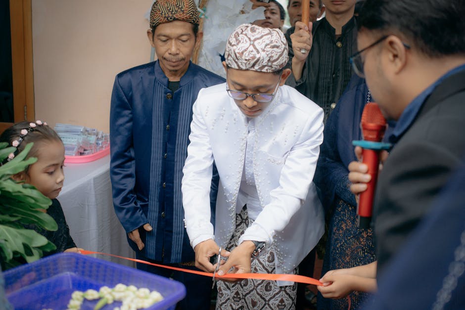 Man in traditional attire cuts ribbon at an indoor event celebration.
