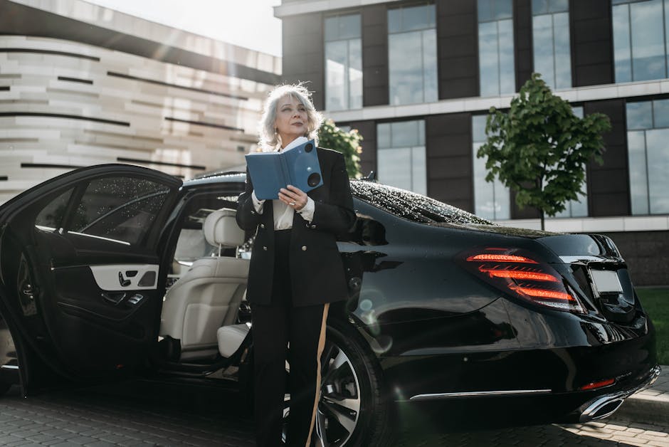 Senior businesswoman exits a black luxury car, holding documents near modern office building.
