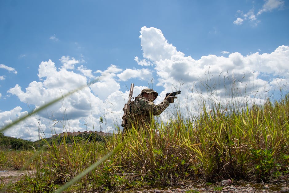 Soldier in camouflage navigating grassy field under clear blue sky, perfect for tactical and military themes.
