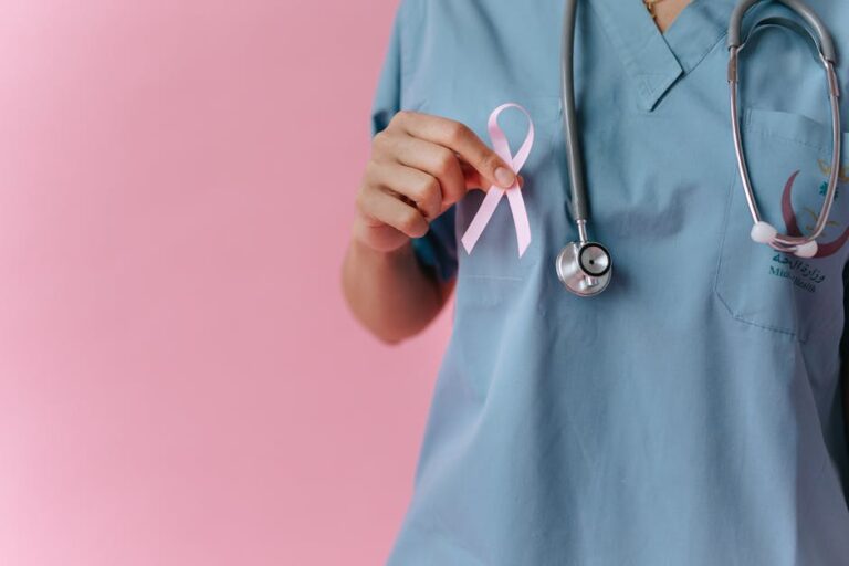 Healthcare worker in scrubs holds a pink breast cancer awareness ribbon symbolizing support.