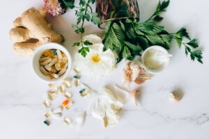 A flatlay of herbal supplements with fresh ginger, garlic, and leaves.