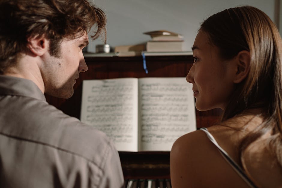 A couple sits close, sharing a romantic moment at the piano indoors, creating a serene atmosphere.
