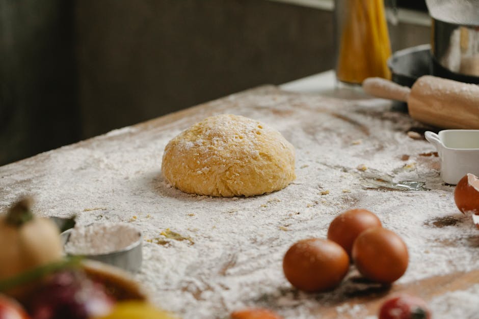 From above of raw dough placed on table covered with flour near kitchen utensils and eggs in kitchen with ingredients