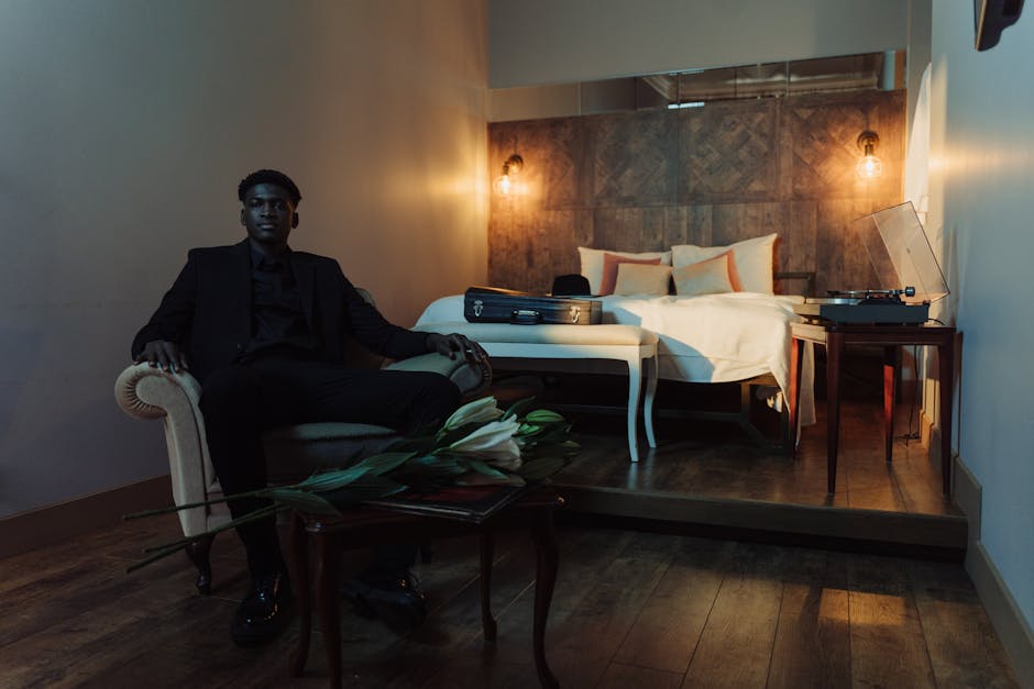 Stylish man in a suit sitting in an armchair in a modern bedroom setting, offering a chic interior look.