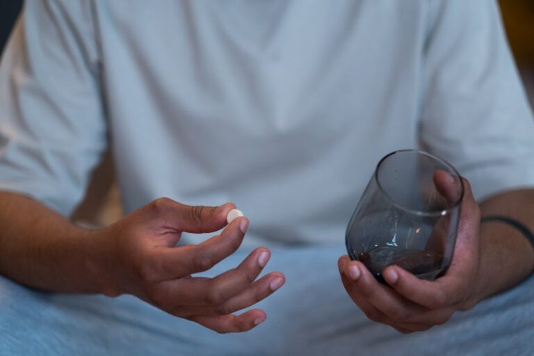 Close-up of an unrecognizable man taking a pill with a glass. Indoor setting.