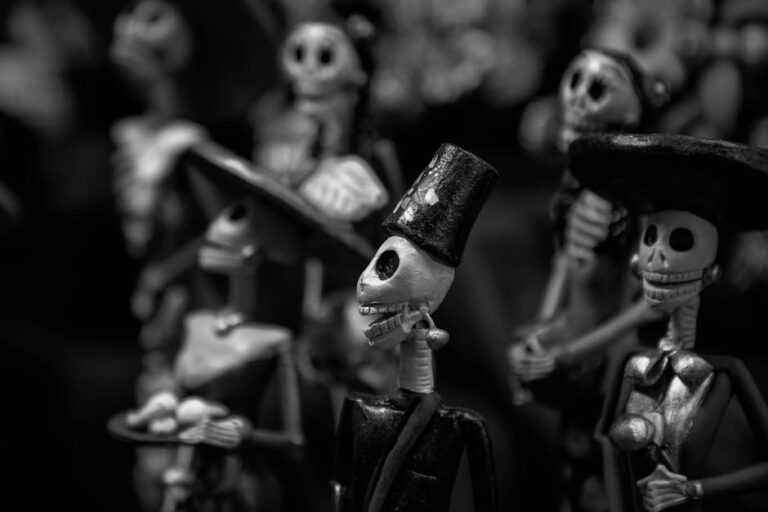 Artistic black and white photo of Día de los Muertos skeleton figures with top hats.