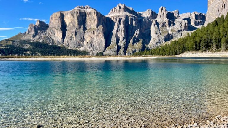 Crystal clear alpine lake with stunning mountains reflecting under a blue sky.