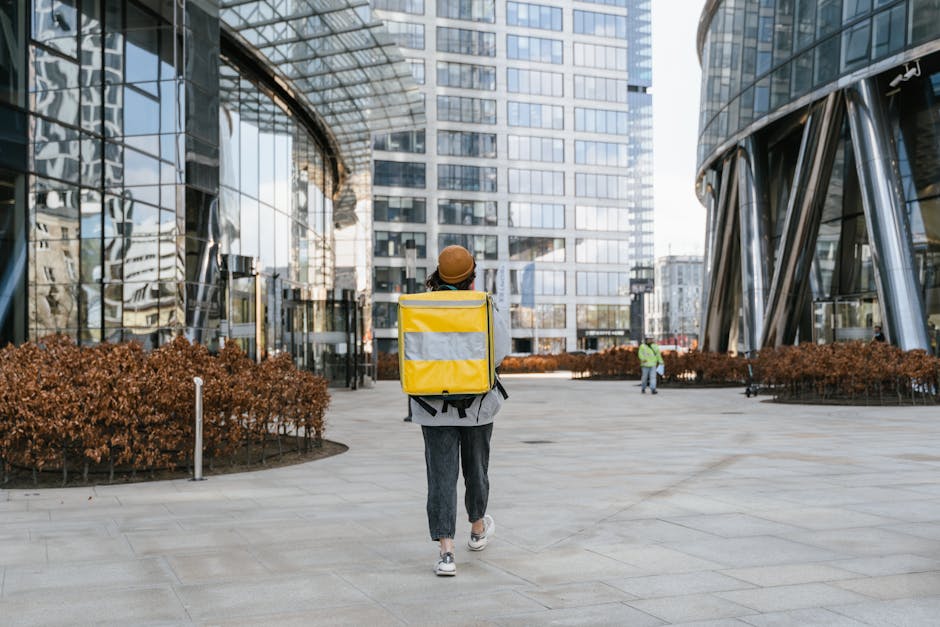 A delivery person with a yellow backpack walking through a modern urban cityscape, ready for service.