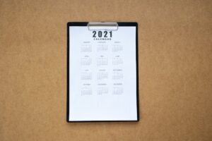 Top-down view of a minimalist 2021 calendar on a clipboard with brown background.