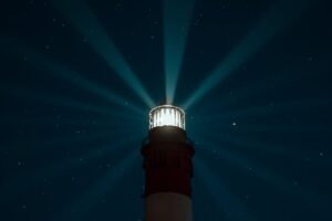 A lighthouse beams light across a starry night sky, creating an ethereal glow over the sea.