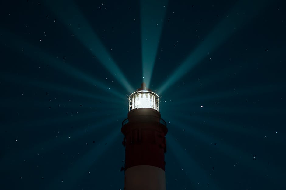 A lighthouse beams light across a starry night sky, creating an ethereal glow over the sea.