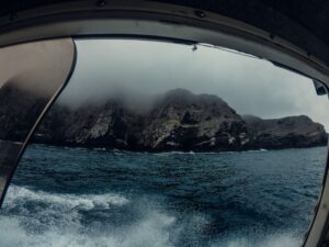 Scenic view of rocky island with mist from a boat. Dramatic and moody seascape.
