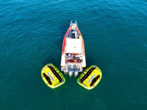 A vibrant aerial view of a boat with attached inflatable water tubes floating on clear blue ocean waters.