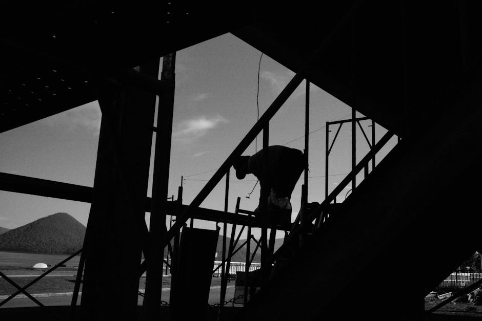 A silhouetted worker bends over a construction frame, with a mountain in the background.