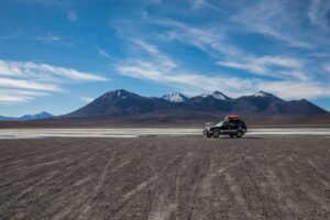Explore the stunning desert landscape of Uyuni, Bolivia with an SUV under a bright blue sky.