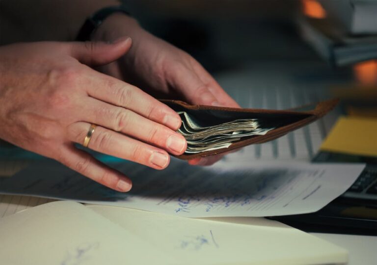Hands holding an open wallet filled with cash above documents, indicating financial planning or budgeting.